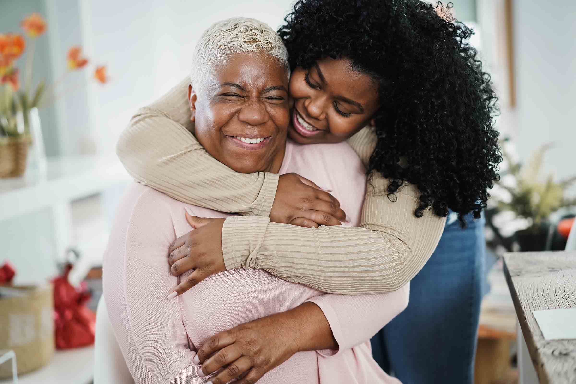 African American daughter hugging her mum indoors at home - Main focus on senior woman face